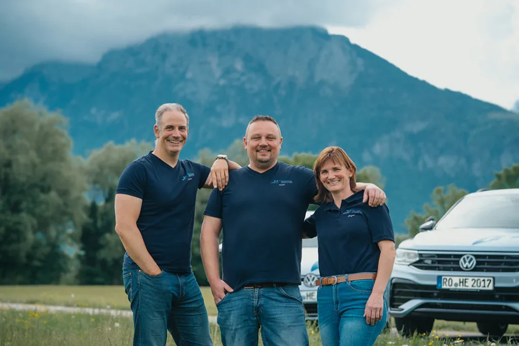 Fahrlehrer-Team der Fahrschule Heppel vor dem Wilden Kaiser, dahinter stehen Fahrschulautos.