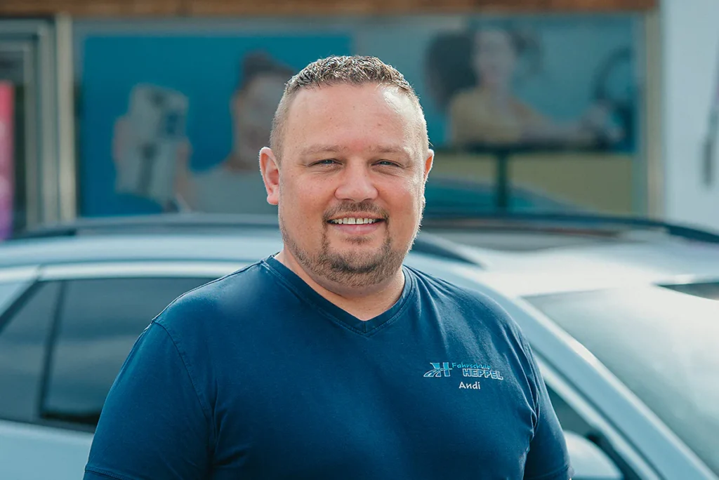 Andreas Heppel, Inhaber der Fahrschule Heppel, steht vor einem Fahrschulauto und lächelt.