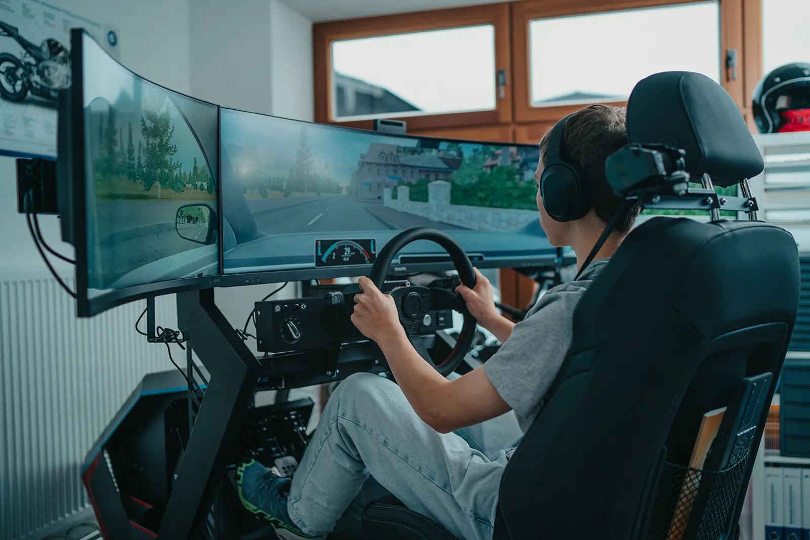 Fahrschüler sitzt mit Kopfhörern am Fahrsimulator der Fahrschule Heppel in Oberaudorf vor drei Bildschirmen.