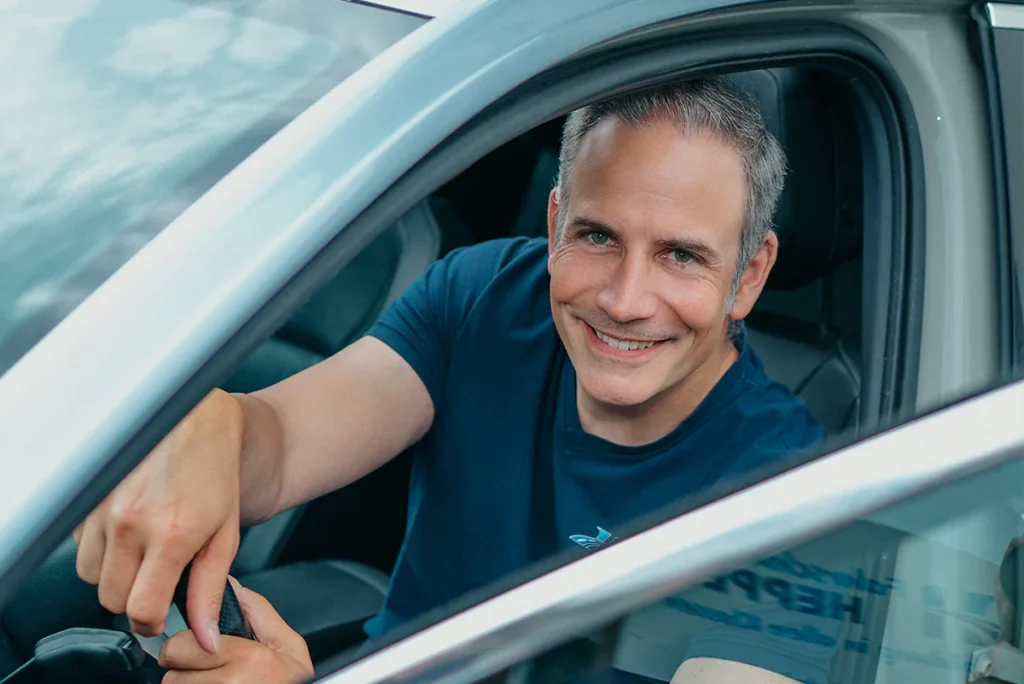 Sascha, Fahrlehrer bei der Fahrschule Heppel, sitzt am Steuer und lächelt aus dem Fenster.