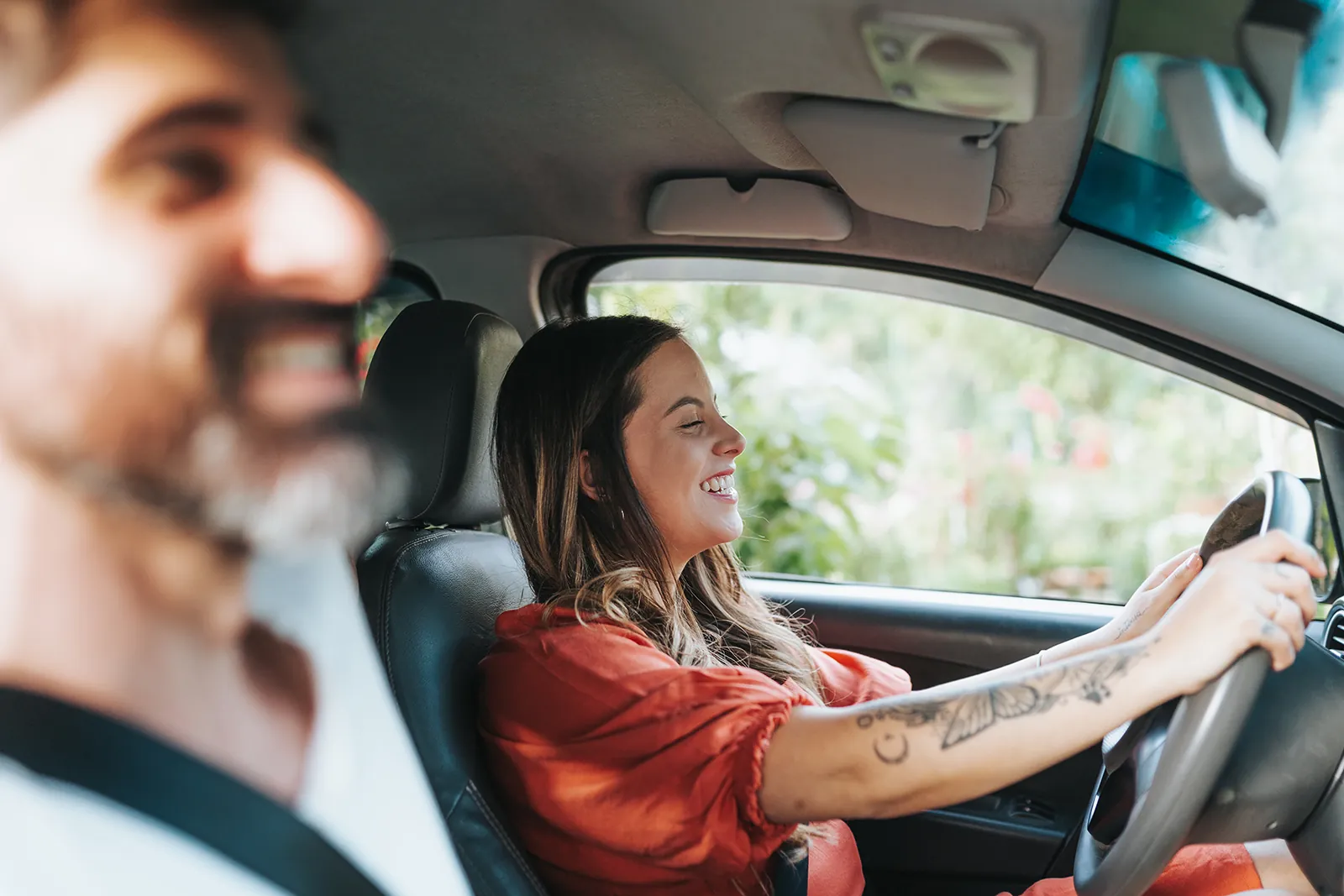 Lachende Frau am Steuer eines Autos, Fahrlehrer im Vordergrund.