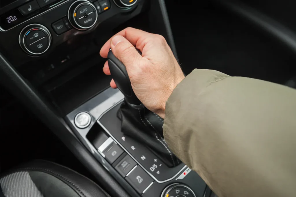 Hand am Automatikschalthebel im Auto, Bedienelemente der Klimaanlage im Hintergrund.