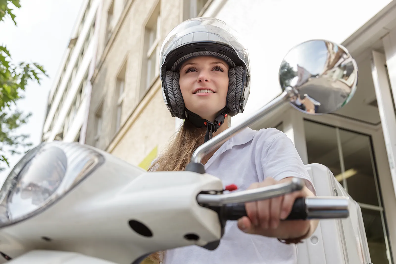 Junge Frau mit Helm auf weißem Motorroller in der Stadt.