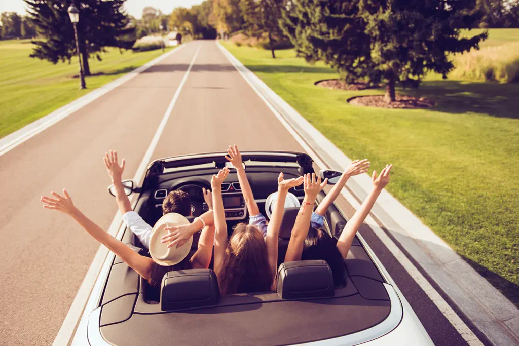 Vier Freunde strecken jubelnd die Arme aus einem offenen Cabrio.