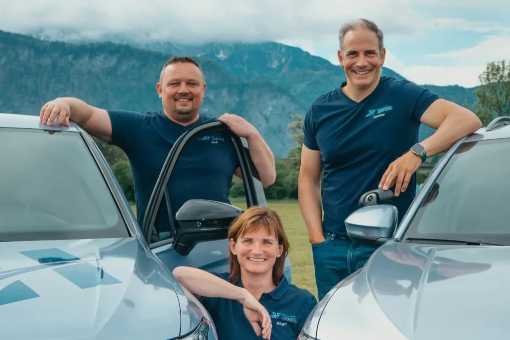 Fahrlehrer-Team der Fahrschule Heppel zwischen zwei Fahrschulautos vor dem Wilden Kaiser.