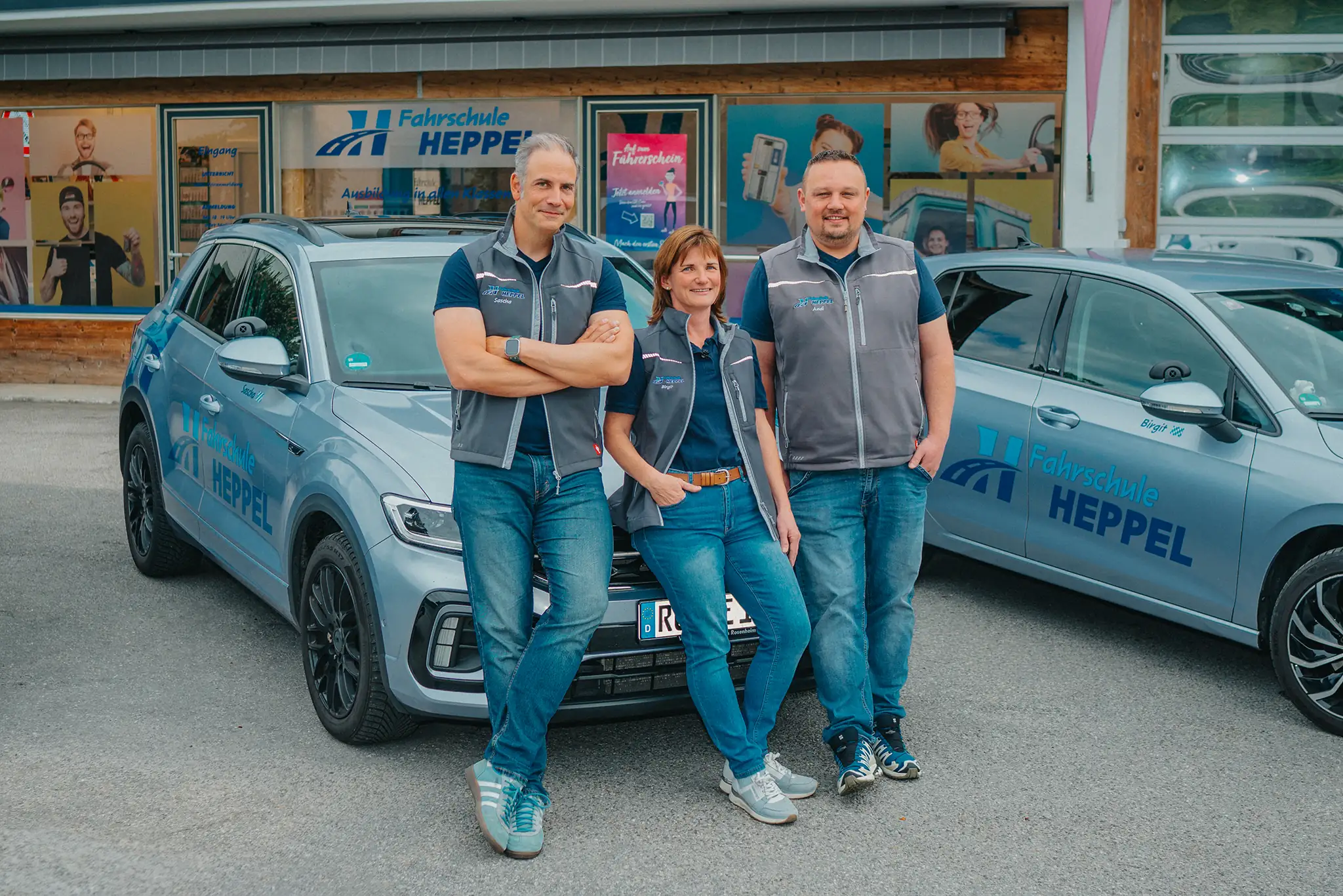 Fahrlehrer-Team der Fahrschule Heppel vor der Filiale in Kiefersfelden, daneben zwei beschriftete Fahrschulautos.